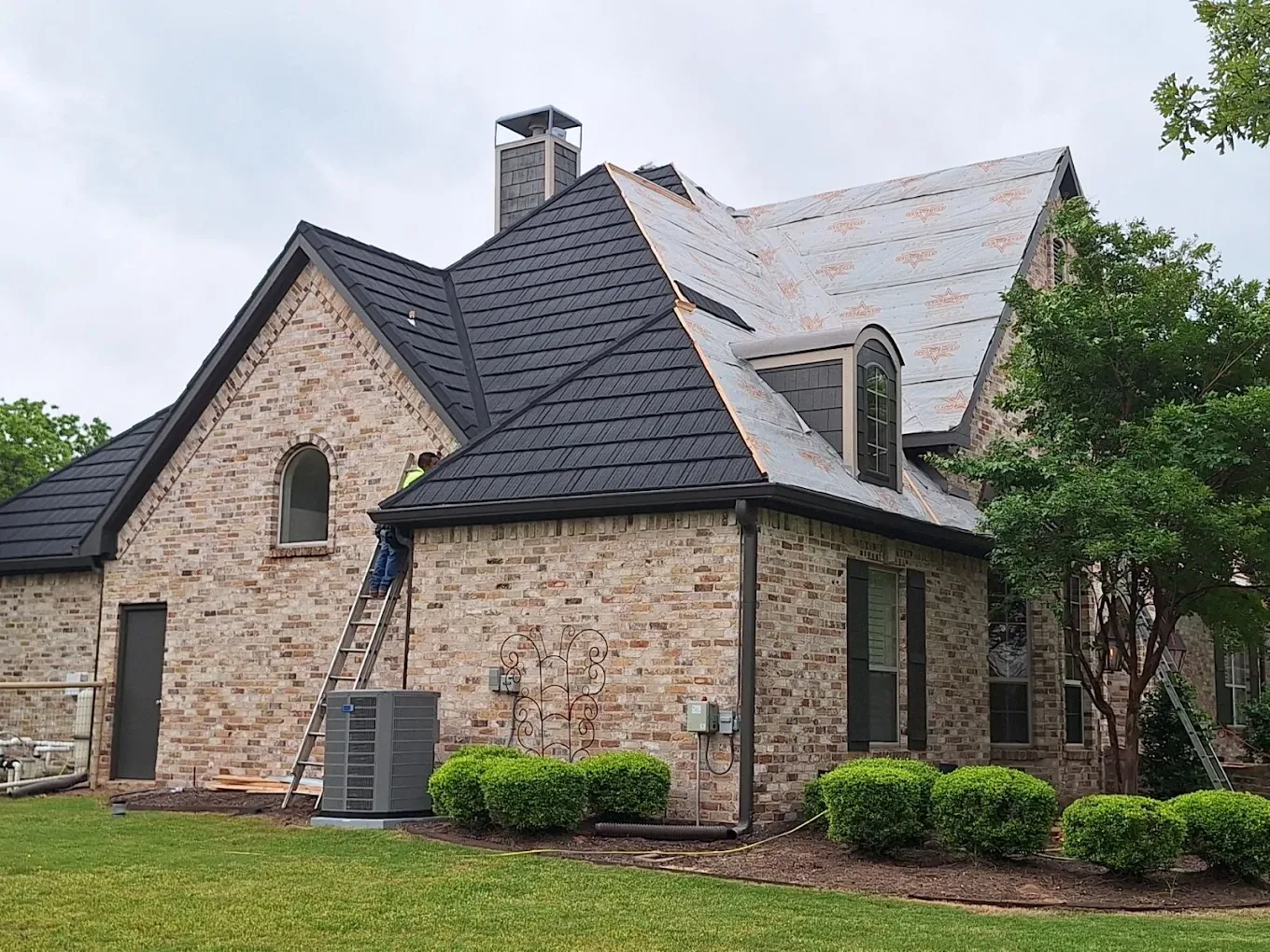 Metal shake roof replacement in progress on a brick home, finished black panels on one elevation and synthetic underlayment exposed on the other